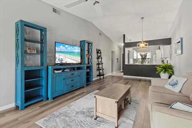 living room featuring ceiling fan, light wood-type flooring, lofted ceiling, and a textured ceiling