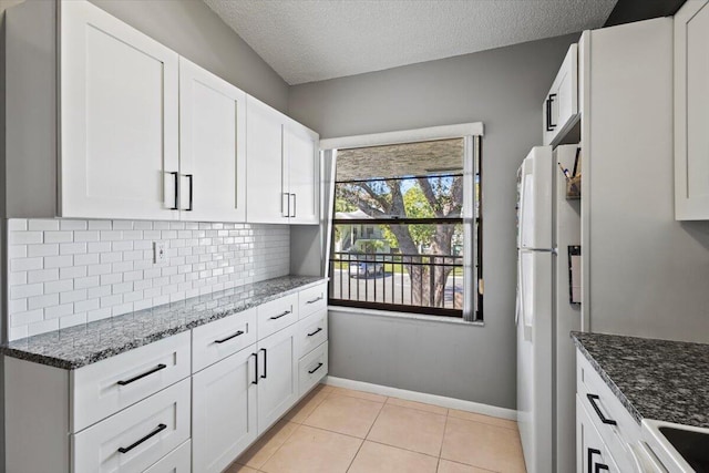 kitchen with white refrigerator, white cabinetry, dark stone counters, and light tile patterned flooring