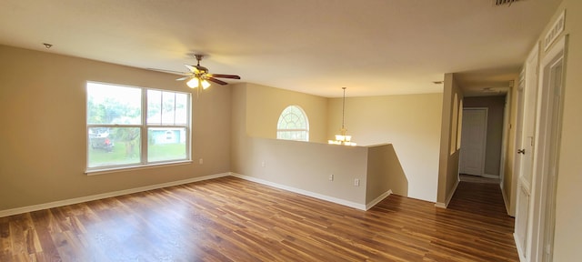 empty room with ceiling fan with notable chandelier and dark wood-type flooring