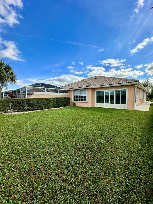 rear view of property featuring glass enclosure and a lawn