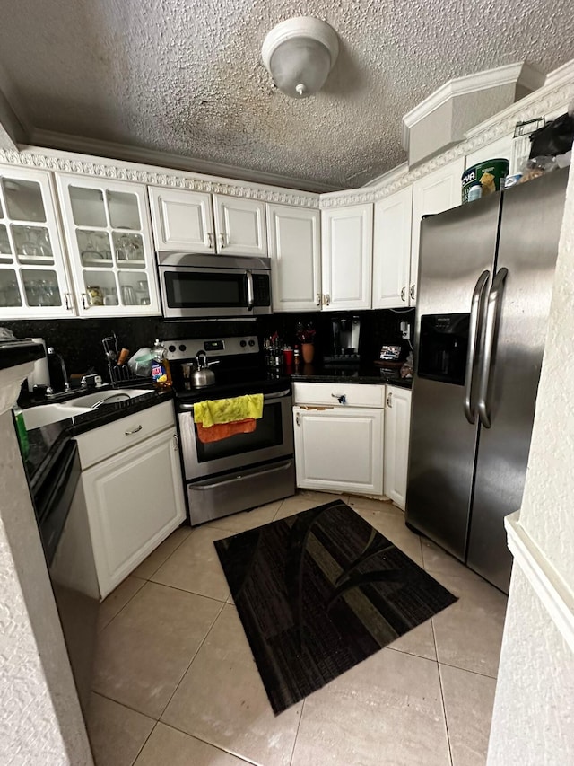 kitchen with ornamental molding, a textured ceiling, stainless steel appliances, light tile patterned floors, and white cabinets