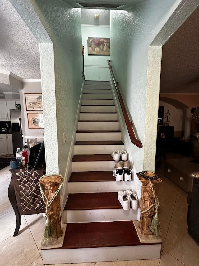 staircase featuring tile patterned flooring, ornamental molding, and a textured ceiling