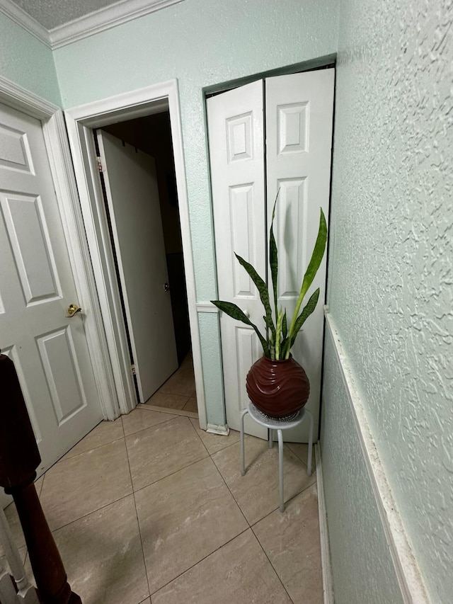 hallway with light tile patterned flooring, ornamental molding, and a textured ceiling