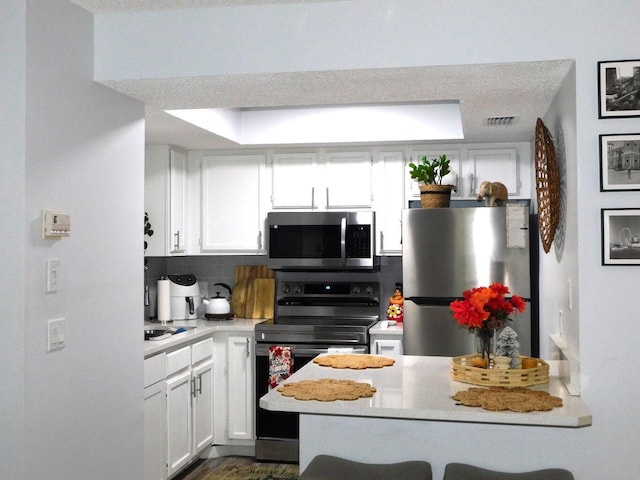 kitchen with stainless steel appliances, a kitchen breakfast bar, tasteful backsplash, white cabinets, and kitchen peninsula