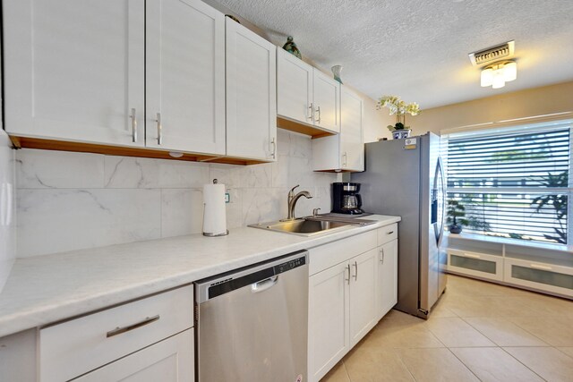 kitchen featuring appliances with stainless steel finishes, sink, light tile patterned floors, white cabinetry, and hanging light fixtures