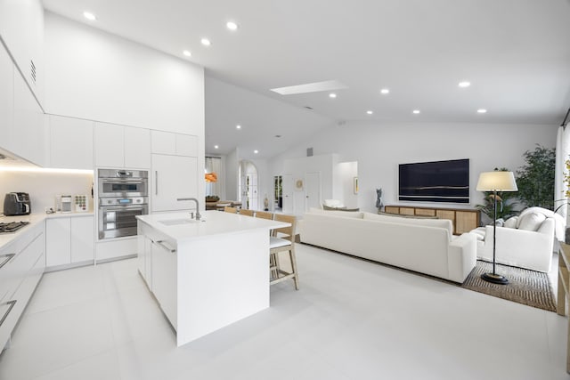 kitchen with an island with sink, stainless steel double oven, white cabinets, a kitchen breakfast bar, and sink