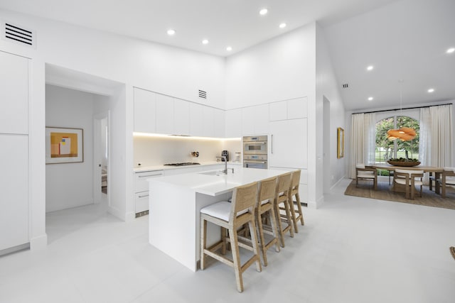 kitchen with sink, white cabinets, a kitchen bar, gas stovetop, and a kitchen island with sink