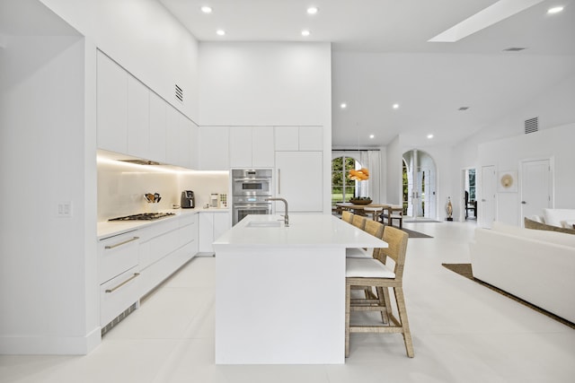 kitchen with appliances with stainless steel finishes, an island with sink, a kitchen bar, white cabinets, and sink