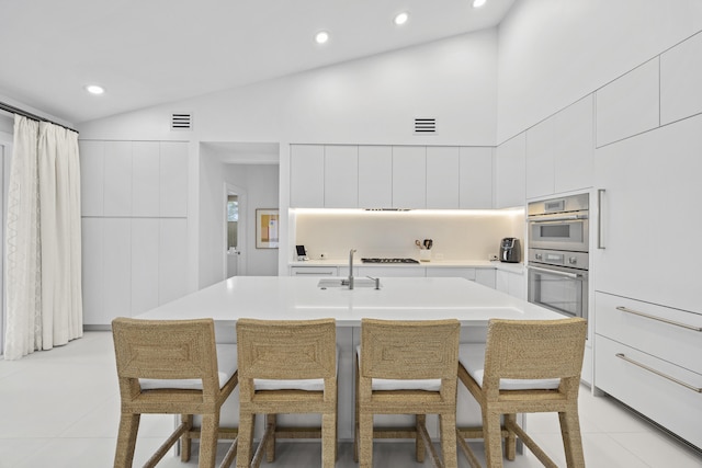 kitchen with a kitchen bar, a kitchen island with sink, white cabinetry, and stainless steel double oven