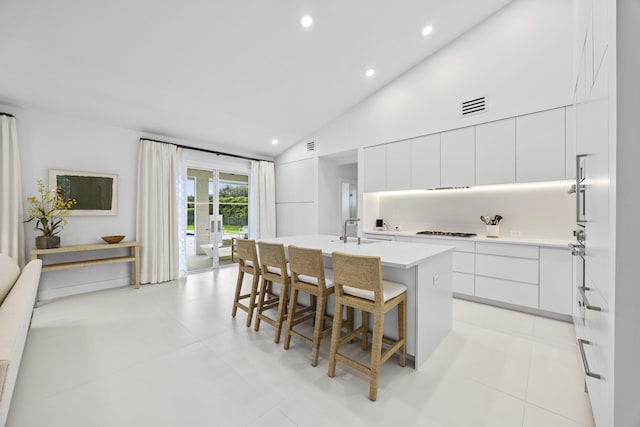 kitchen with a center island with sink, gas cooktop, lofted ceiling, white cabinetry, and a kitchen breakfast bar