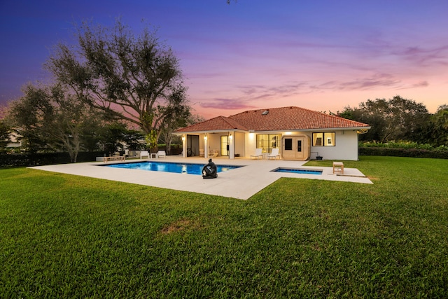 back house at dusk with a patio area, a swimming pool with hot tub, and a yard