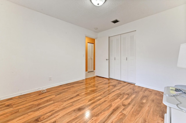 unfurnished bedroom featuring light wood-type flooring, a textured ceiling, and a closet