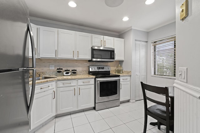 kitchen featuring light tile patterned flooring, ornamental molding, stainless steel appliances, decorative backsplash, and white cabinets