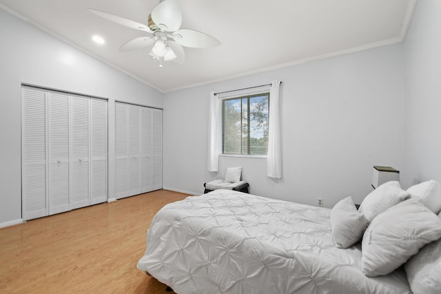 bedroom with vaulted ceiling, hardwood / wood-style flooring, ceiling fan, multiple closets, and crown molding