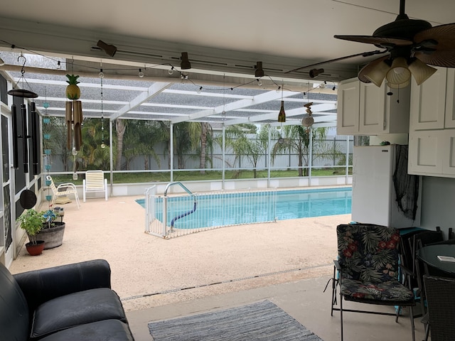 view of swimming pool featuring glass enclosure, a patio area, and ceiling fan