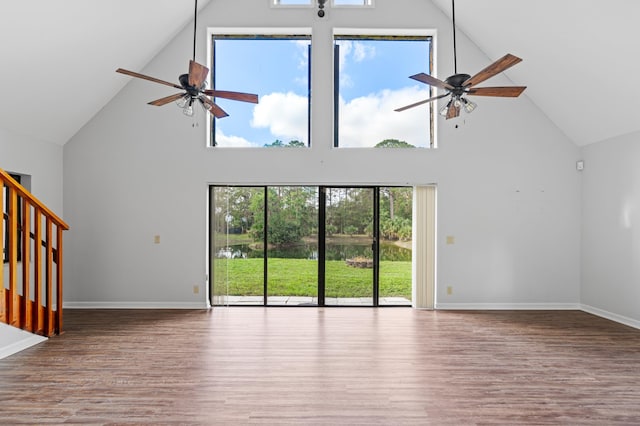 unfurnished living room featuring ceiling fan, hardwood / wood-style floors, and a towering ceiling