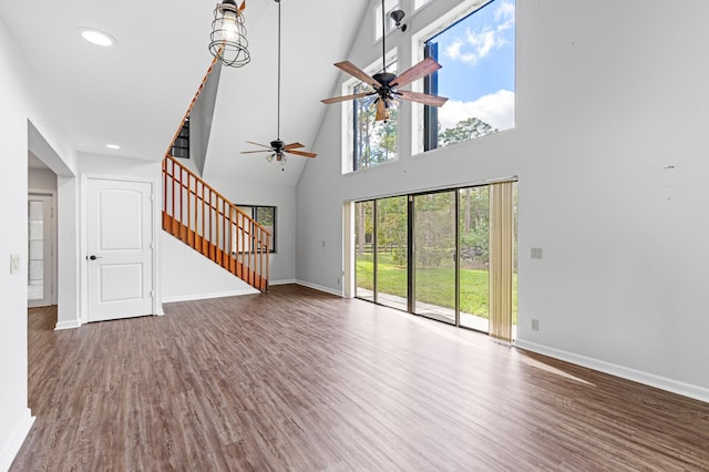 unfurnished living room featuring a towering ceiling, hardwood / wood-style flooring, and ceiling fan