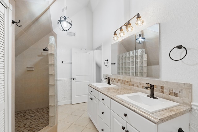 bathroom featuring vaulted ceiling, tiled shower, tile patterned flooring, backsplash, and vanity