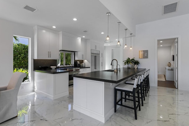 kitchen with pendant lighting, an island with sink, sink, white cabinets, and high end appliances