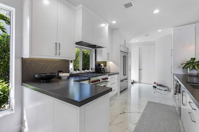 kitchen with high end appliances, white cabinetry, tasteful backsplash, and kitchen peninsula