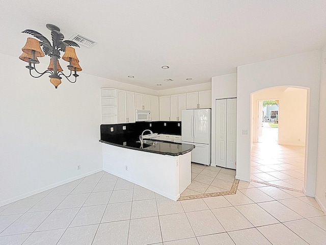 kitchen featuring kitchen peninsula, white appliances, light tile patterned floors, a notable chandelier, and white cabinetry