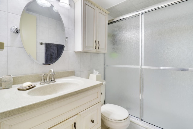 bathroom featuring vanity, a shower with door, backsplash, toilet, and tile walls