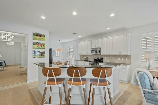 kitchen featuring a center island, decorative backsplash, light tile patterned floors, appliances with stainless steel finishes, and white cabinets