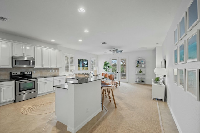 kitchen featuring a kitchen island with sink, white cabinets, a kitchen bar, and appliances with stainless steel finishes