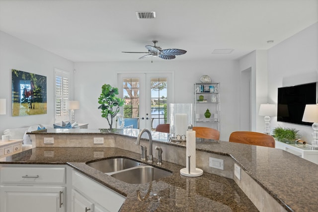 kitchen featuring white cabinets, dark stone counters, french doors, sink, and ceiling fan