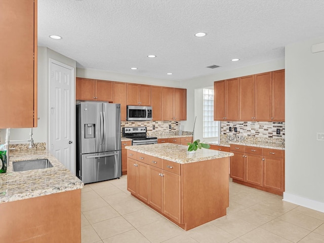 kitchen with sink, stainless steel appliances, light stone counters, decorative backsplash, and a kitchen island