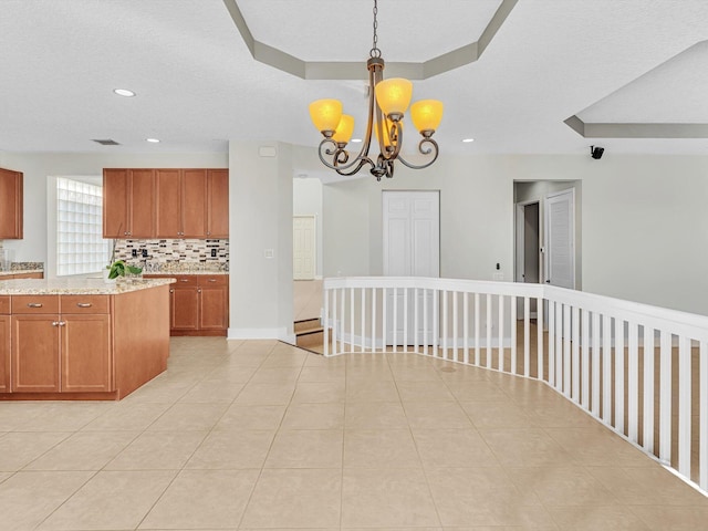 kitchen with a tray ceiling, backsplash, pendant lighting, and a notable chandelier