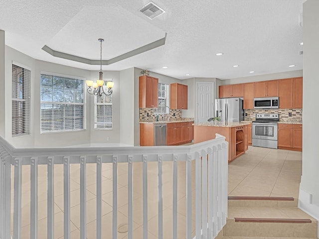 kitchen with stainless steel appliances, light tile patterned floors, backsplash, decorative light fixtures, and a kitchen island