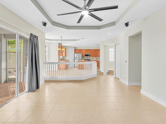 unfurnished living room featuring ceiling fan with notable chandelier, light tile patterned floors, a textured ceiling, and a tray ceiling