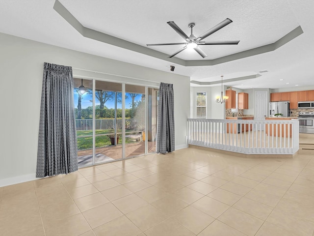 unfurnished living room with ceiling fan with notable chandelier, a raised ceiling, light tile patterned floors, and a textured ceiling