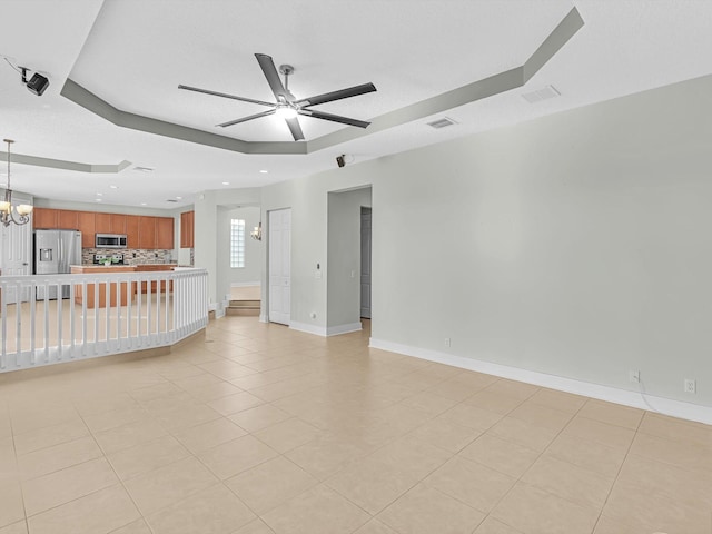 unfurnished living room featuring ceiling fan with notable chandelier, a raised ceiling, and light tile patterned flooring