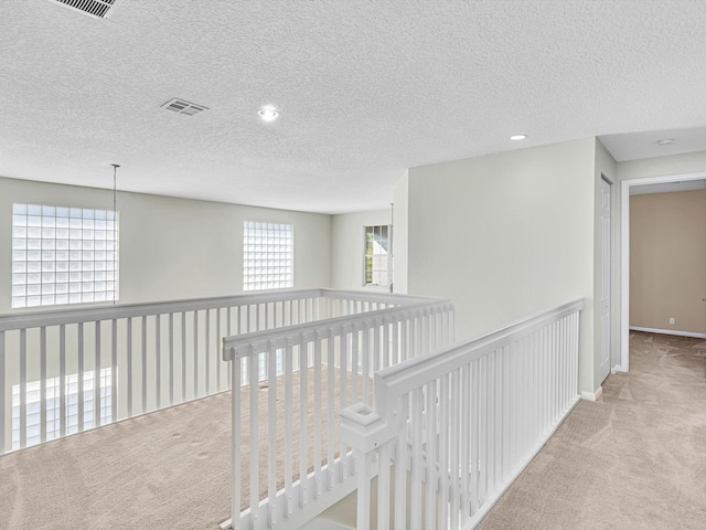 hall with light carpet and a textured ceiling