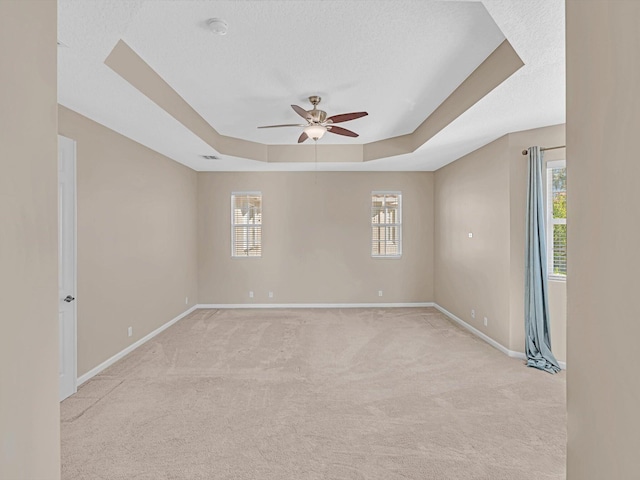 carpeted empty room with a textured ceiling, a raised ceiling, and ceiling fan