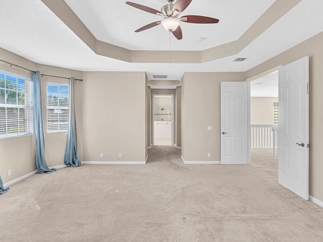 carpeted spare room with ceiling fan and a tray ceiling