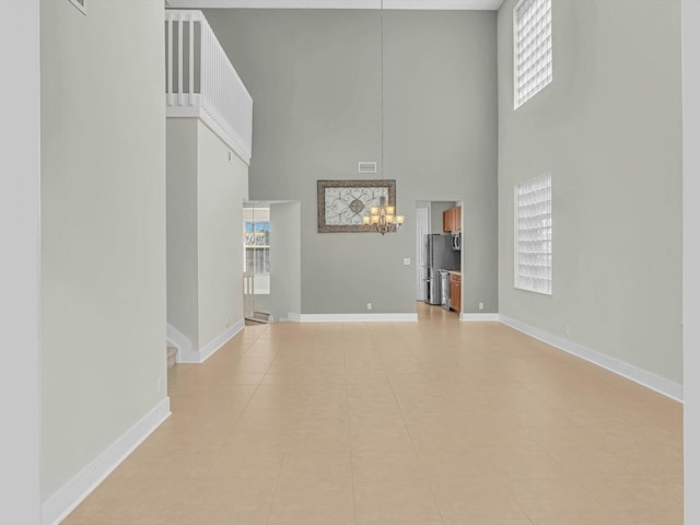 unfurnished living room with plenty of natural light, a towering ceiling, a chandelier, and light tile patterned floors