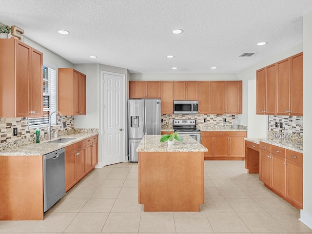 kitchen with appliances with stainless steel finishes, light stone counters, sink, light tile patterned floors, and a kitchen island