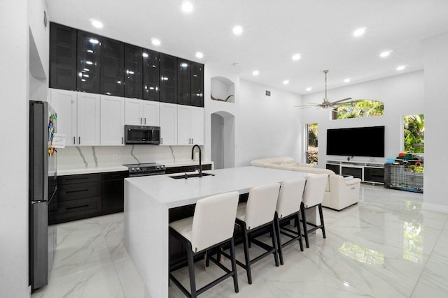 kitchen featuring sink, a kitchen breakfast bar, backsplash, an island with sink, and appliances with stainless steel finishes