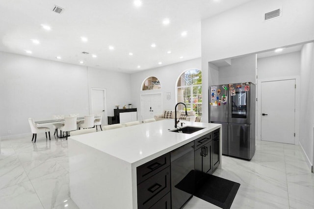 kitchen featuring stainless steel fridge, a kitchen island with sink, and sink