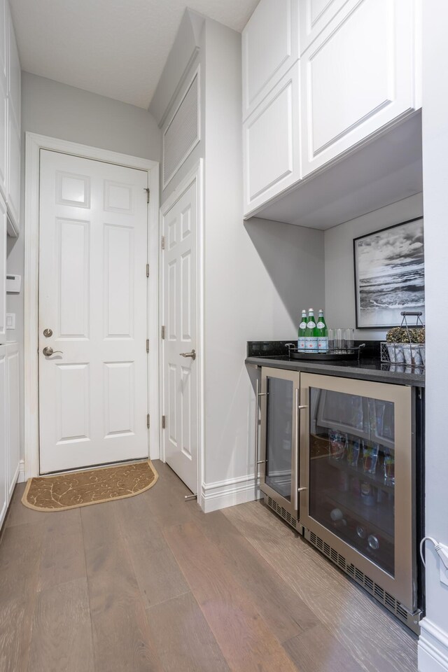 bar with a dry bar, wine cooler, baseboards, and wood finished floors