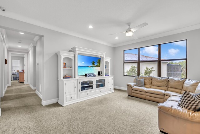 living area featuring light carpet, baseboards, ornamental molding, and a ceiling fan