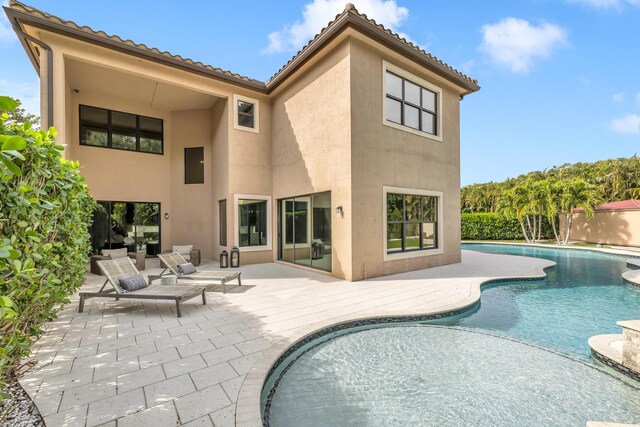 rear view of house with a tile roof, an outdoor pool, a patio, and stucco siding