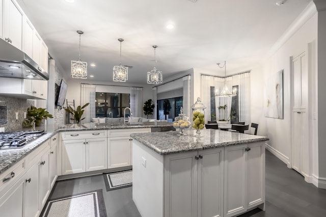 kitchen with kitchen peninsula, pendant lighting, stainless steel gas stovetop, light stone countertops, and white cabinets