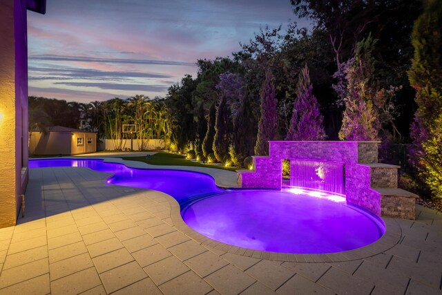 pool at dusk with a patio area, fence, a lawn, and a fenced in pool