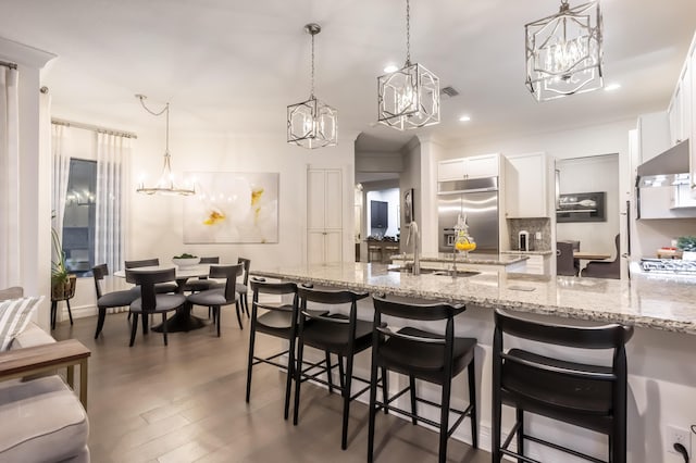 kitchen featuring a kitchen breakfast bar, hanging light fixtures, stainless steel built in fridge, white cabinetry, and a sink