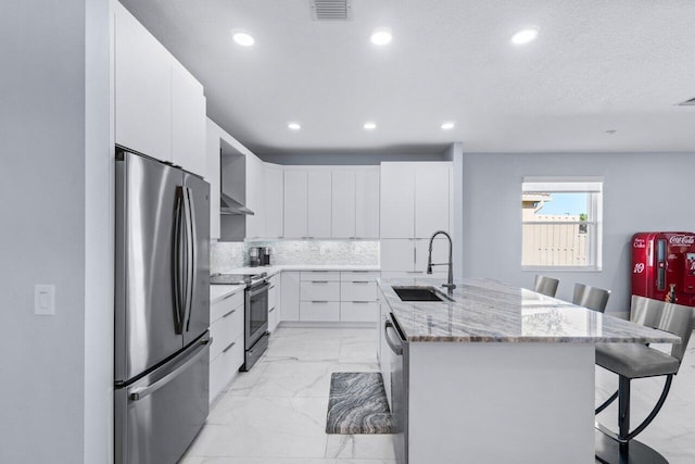 kitchen with a kitchen bar, a kitchen island with sink, white cabinets, appliances with stainless steel finishes, and sink