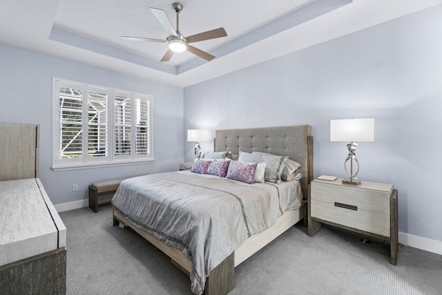 carpeted bedroom with a raised ceiling and ceiling fan